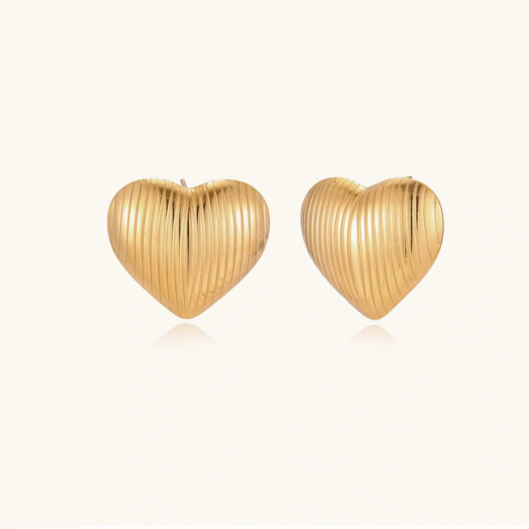Pair of gold heart-shaped stud earrings with vertical ribbed texture on a cream background