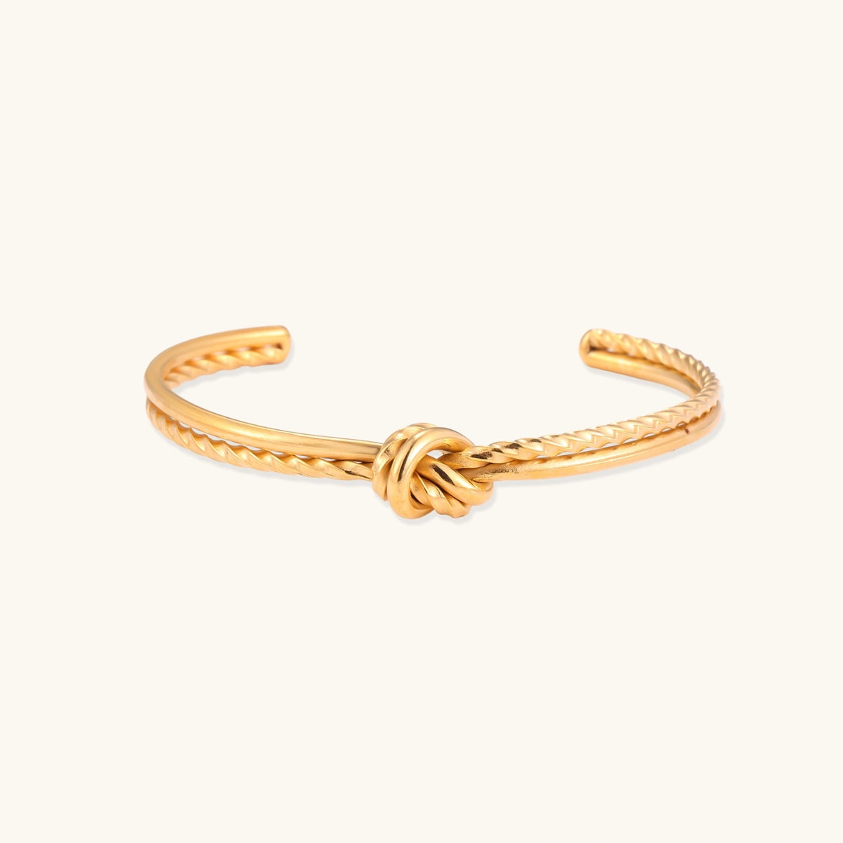 Gold knot cuff bracelet laid flat, showing the smooth and twisted bands meeting at a center knot