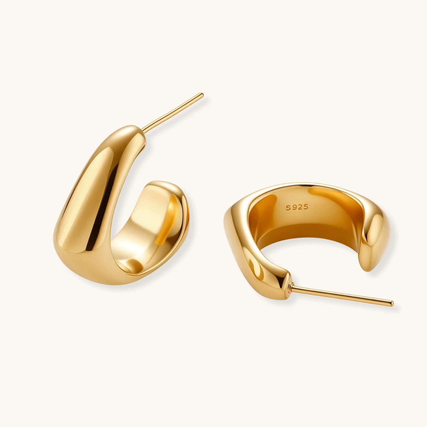 Close-up of curved gold-plated huggie earrings with sculptural design on white background, showing polished finish.