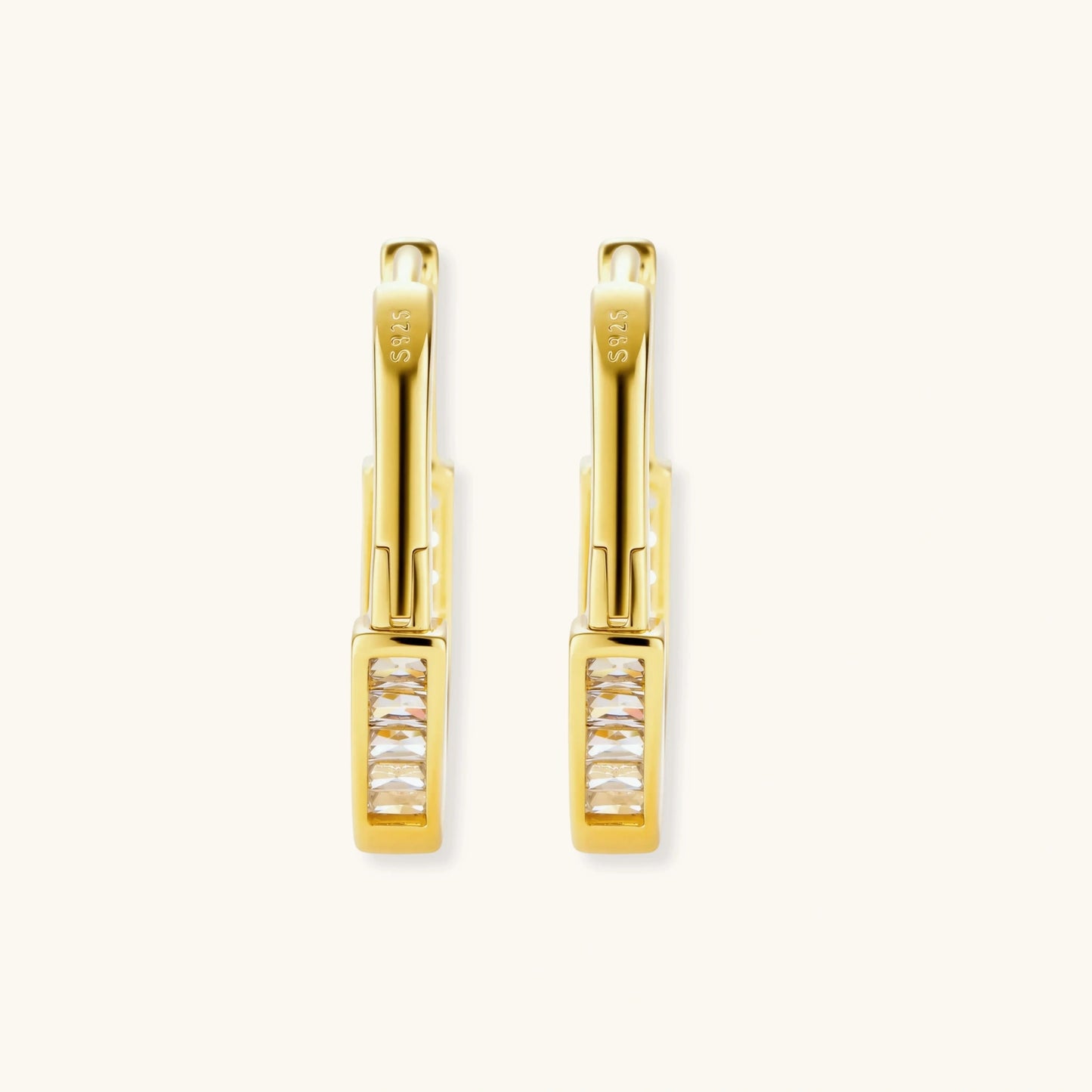 Close-up of gold-plated sterling silver huggie hoop earrings featuring rectangular cubic zirconia stones on neutral background.